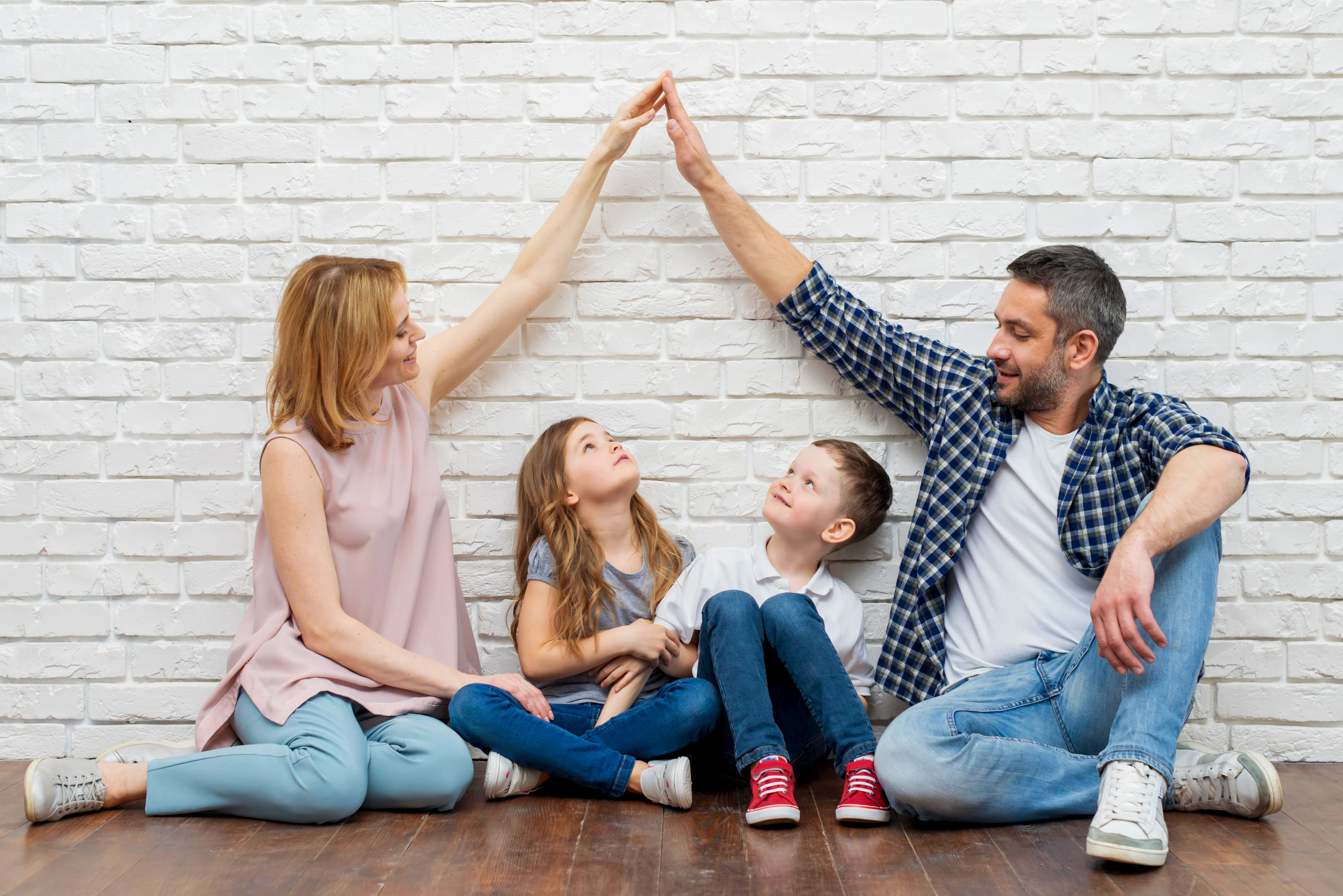 HFK1676 Bild zur Hausratversicherung. Zeigt Eltern, die mit den Händen ein Hausdach über ihren Kindern bilden. 