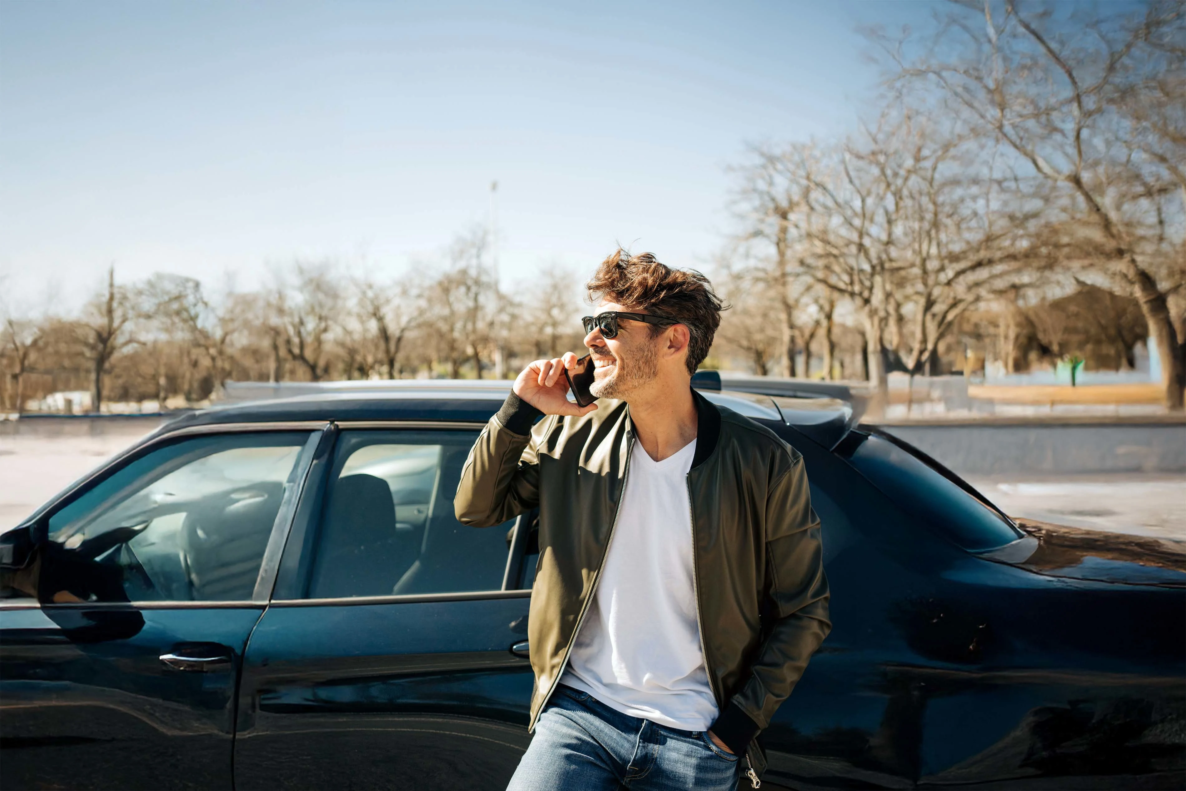 Ein Mann steht telefonierend vor seinem Auto und schaut zur Seite.